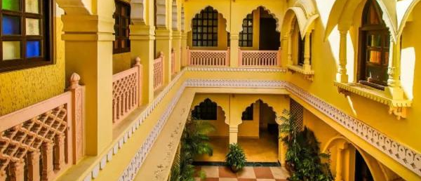 A vibrant yellow courtyard with intricate pink railings and arched windows, bathed in sunlight in Jaipur.