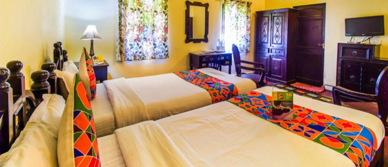 A vibrant hotel room in Jaipur with two beds, colorful textiles, and traditional wooden furniture.