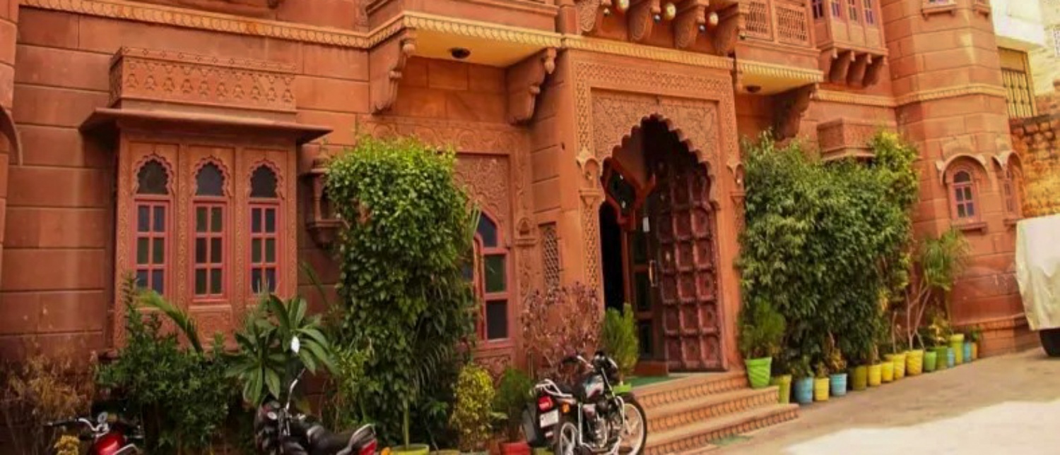 A traditional Indian haveli with intricate red sandstone carvings and potted plants outside in Jodhpur.