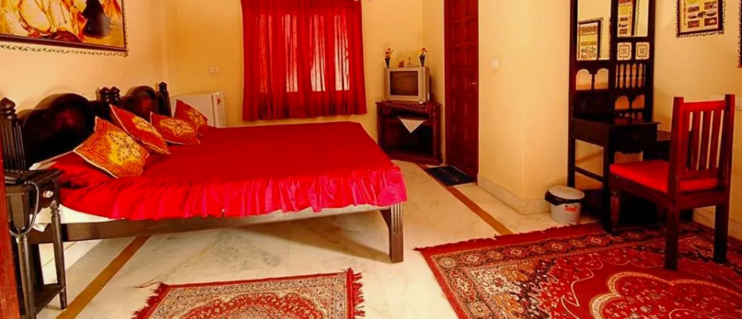 Inviting traditional haveli bedroom in Jodhpur featuring a red bed, matching curtains, and ornate rugs.