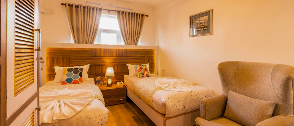 A comfortable hotel room with two single beds, a bedside lamp, and an armchair in Kathmandu.
