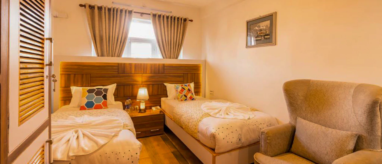 A comfortable hotel room with two single beds, a bedside lamp, and an armchair in Kathmandu.
