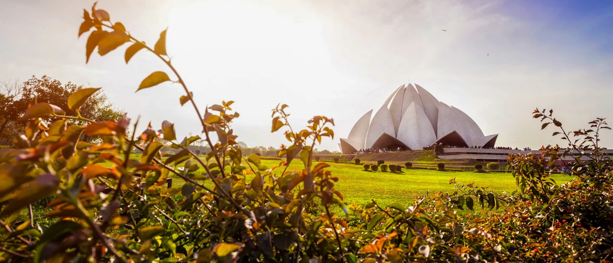 The beautiful Lotus Temple in New Delhi, surrounded by green lawns and sunlit foliage.