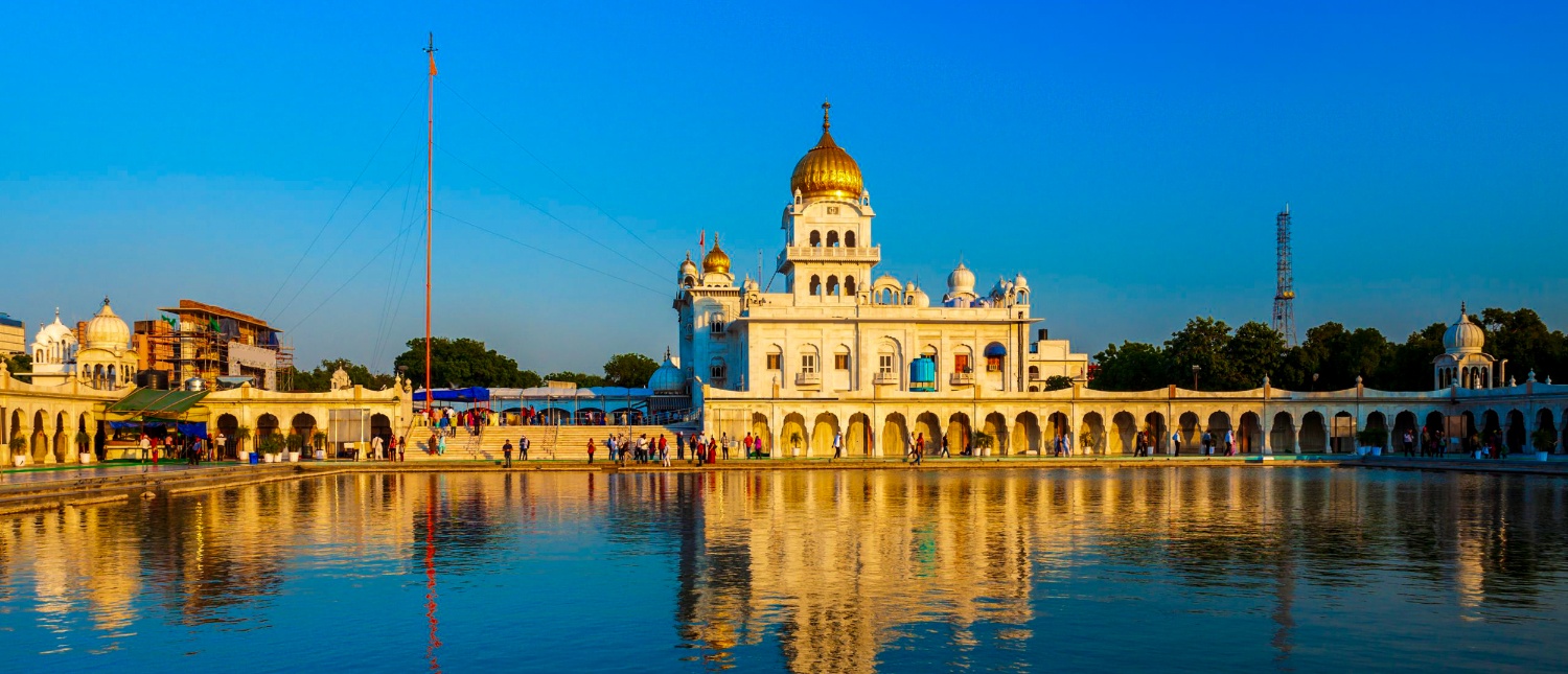 A grand white Sikh temple with a golden dome perfectly reflected in a serene pond in New Delhi.