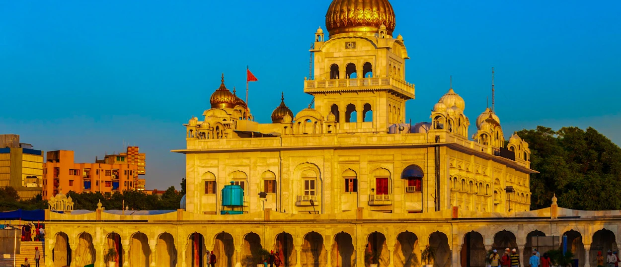 A grand Sikh temple with golden domes and intricate architecture under a clear blue sky in Delhi.