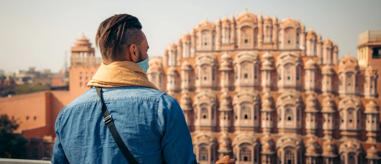 A traveler wearing a mask looks at the ornate pink Hawa Mahal palace in Jaipur.