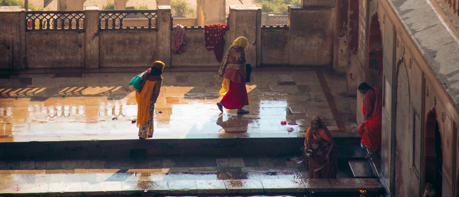 Women in colorful saris walk through a sunlit courtyard of an ornate palace in Jaipur.