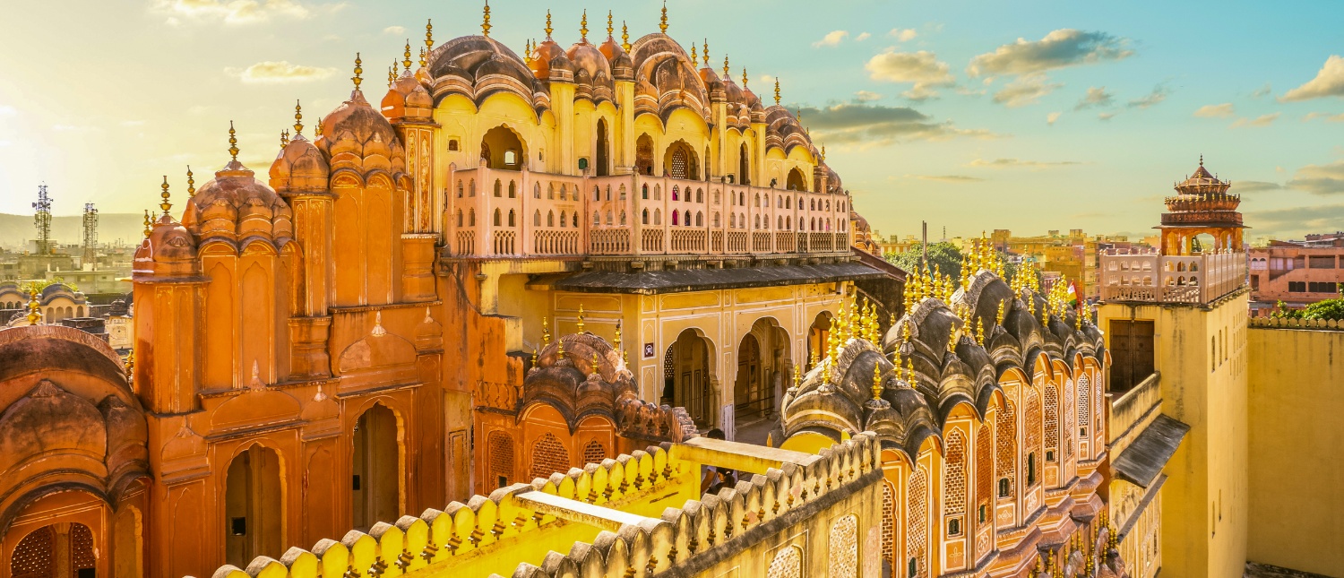 The ornate pink and yellow Hawa Mahal palace in Jaipur under a golden sky.
