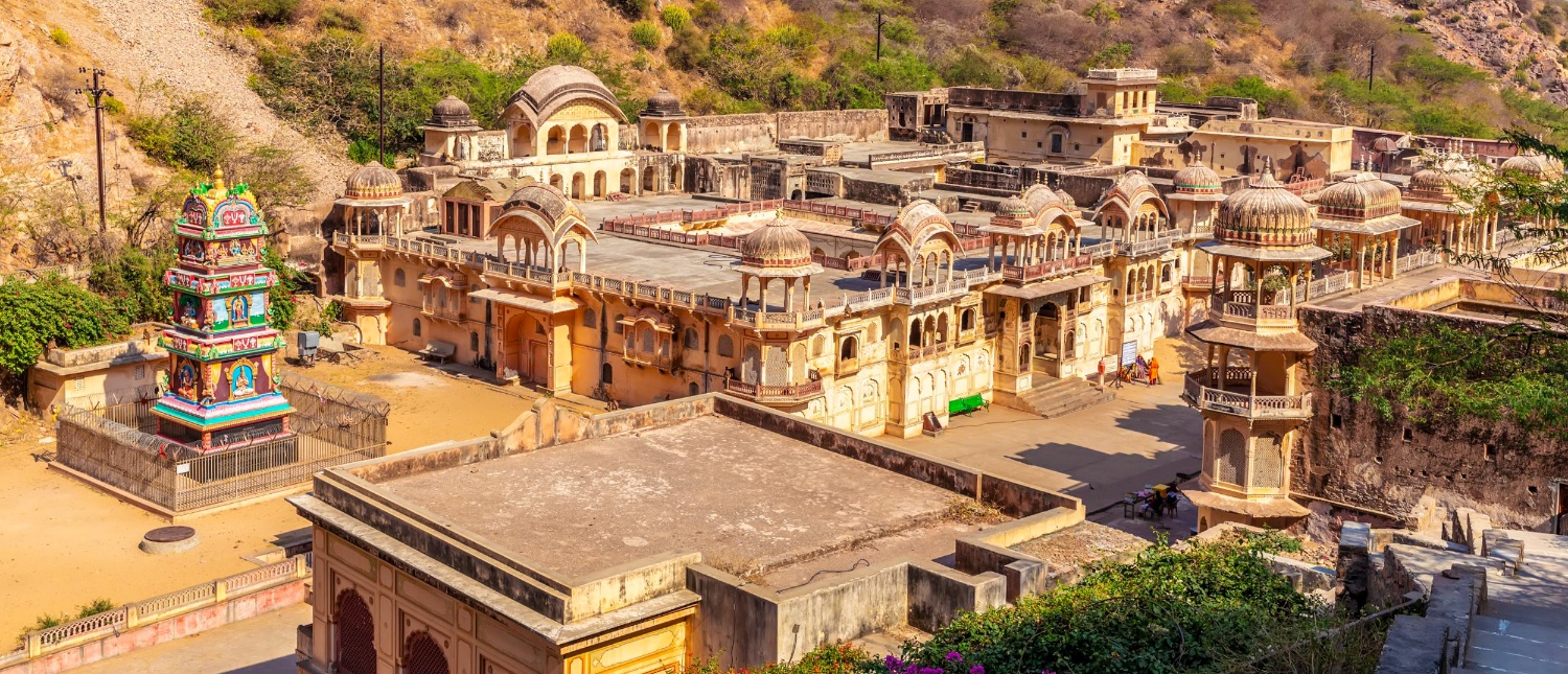 Ornate stone temples and a vibrant shrine spread across a hillside in Jaipur, India.