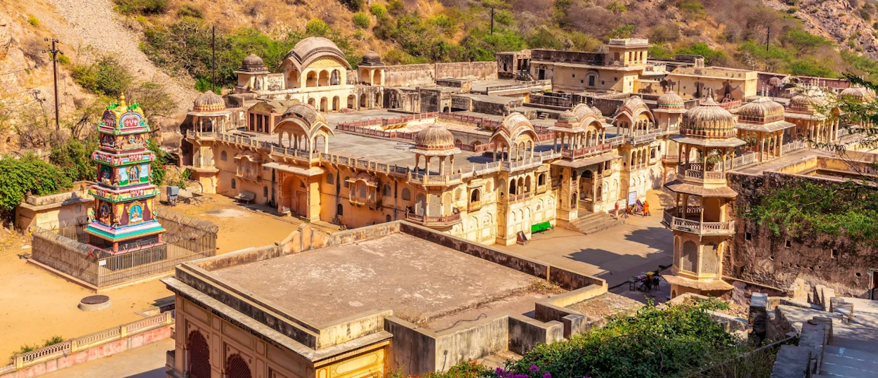 Ornate stone temples and a vibrant shrine spread across a hillside in Jaipur, India.