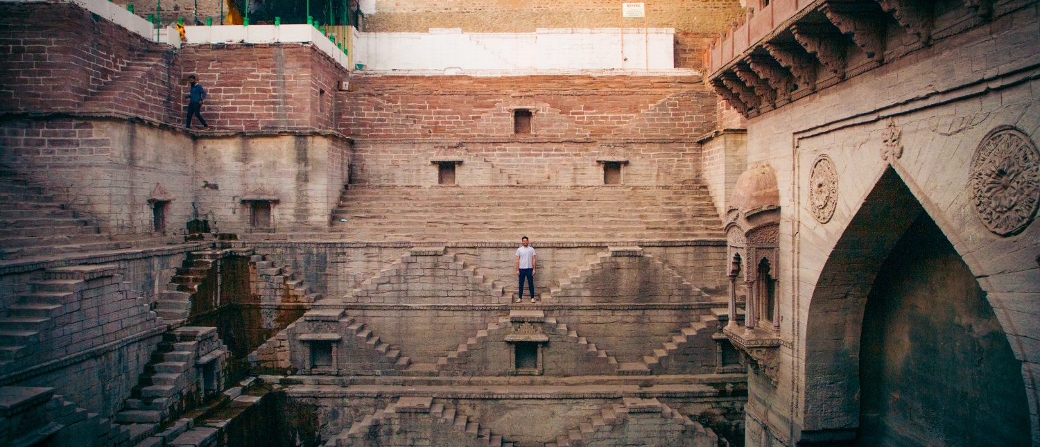 A lone figure stands on the intricate steps of a historic stone stepwell in Jodhpur.