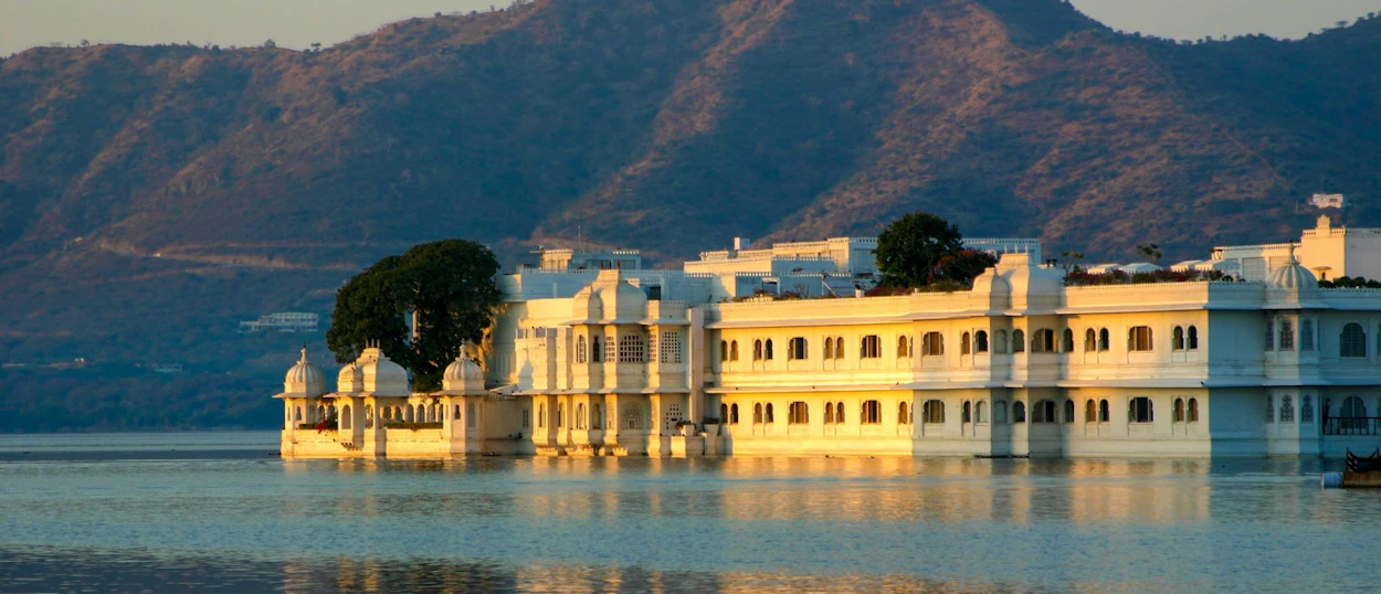 The elegant white palace of Udaipur glows softly on Lake Pichola during a serene sunset.