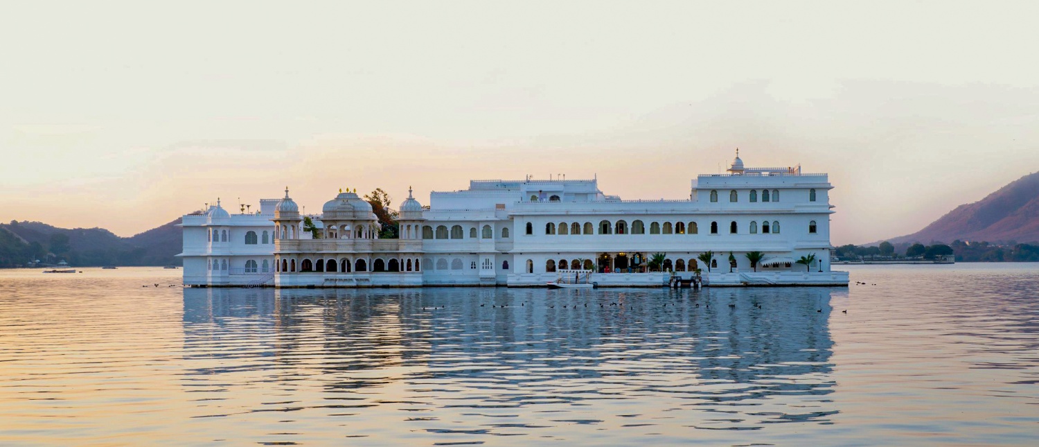 A majestic white palace floats on the calm waters of Lake Pichola at sunset in Udaipur.