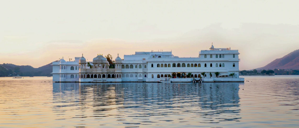 A majestic white palace floats on the calm waters of Lake Pichola at sunset in Udaipur.