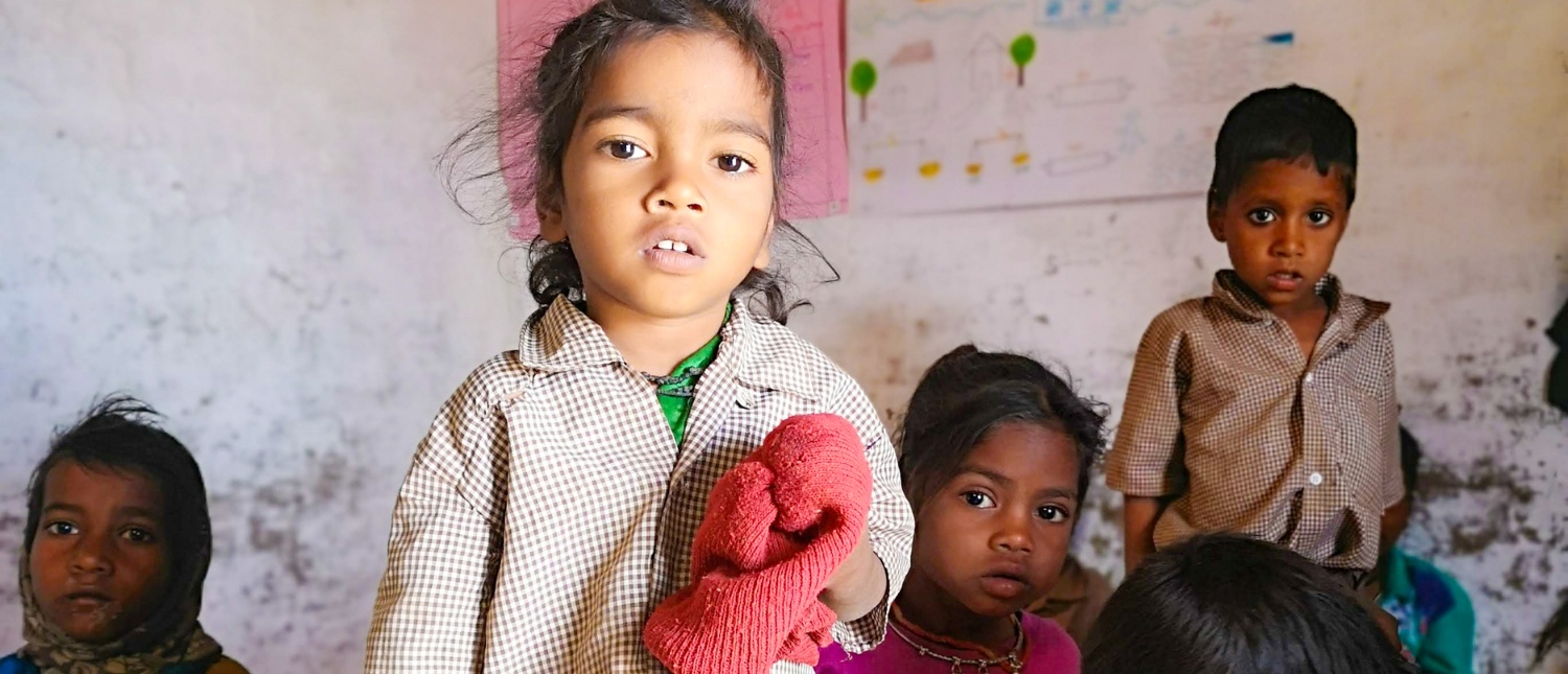 Four young children, including a girl holding a red cloth, look curiously at the camera.