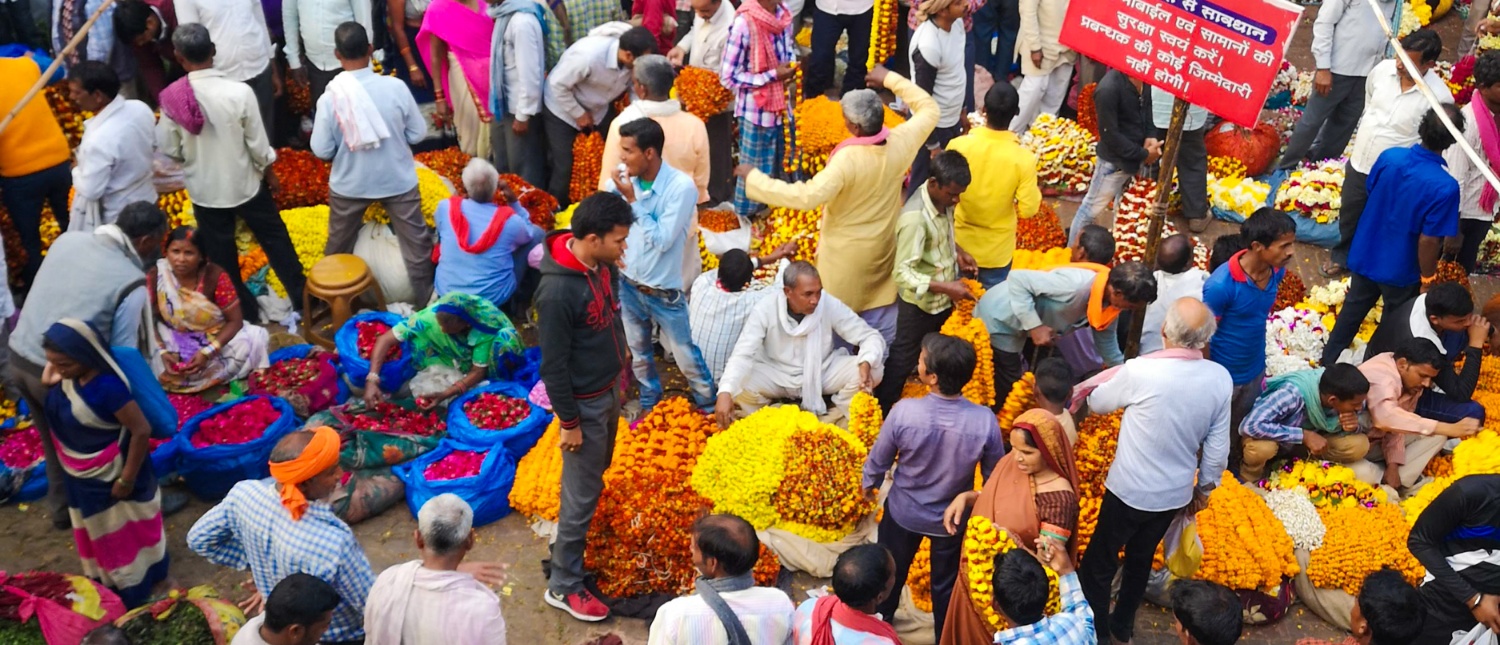 A bustling flower market in Udaipur with many people buying and selling colorful marigolds.