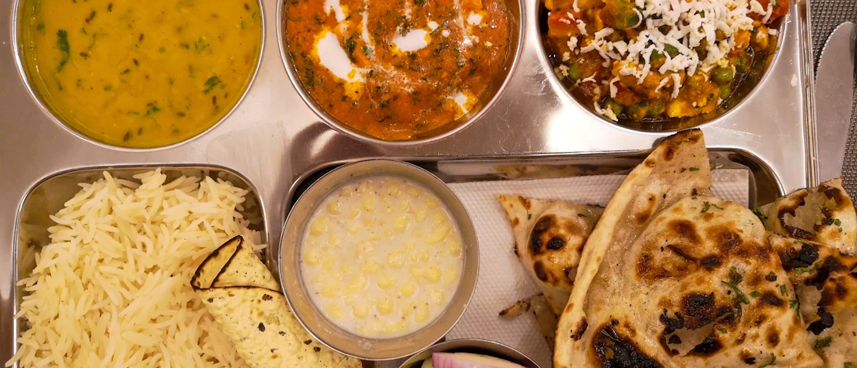 An appetizing North Indian thali meal with dal, curries, basmati rice, raita, and naan.