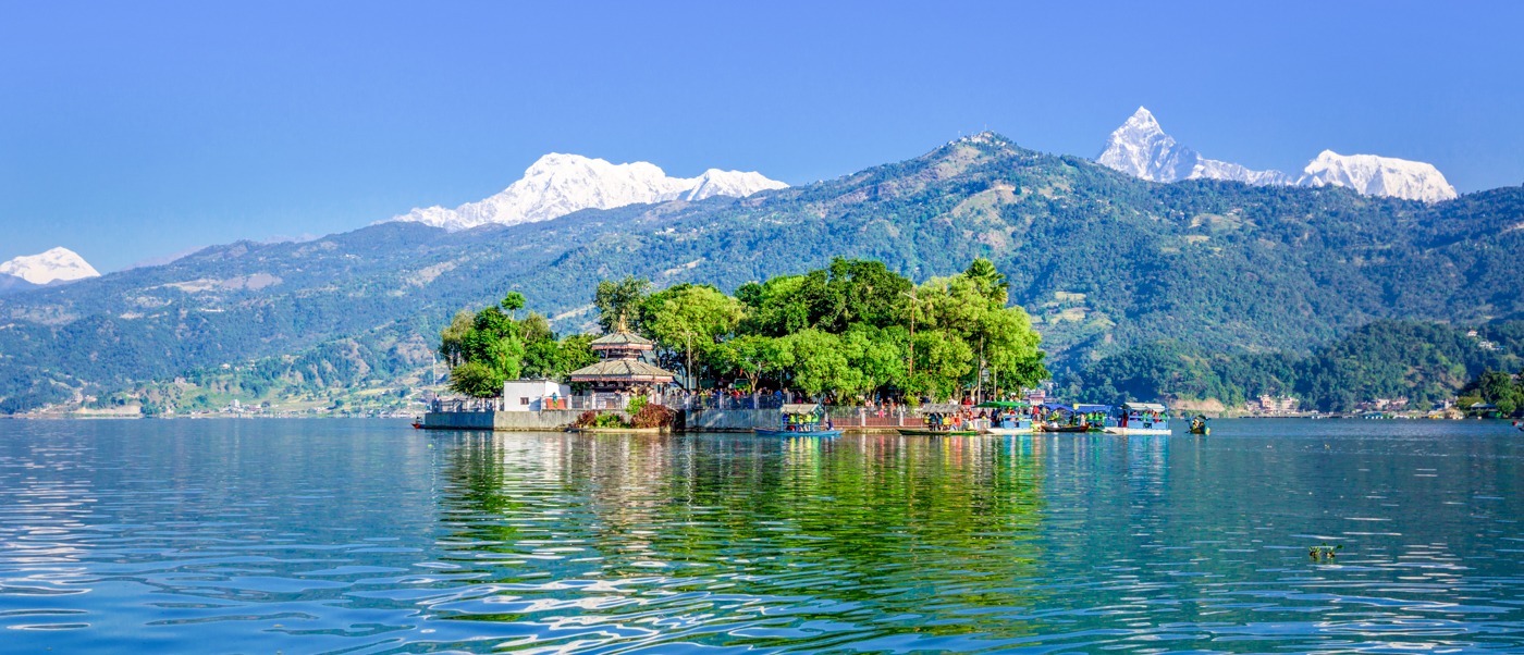 Serene Phewa Lake in Pokhara with Tal Barahi Temple on an island and towering Himalayas.
