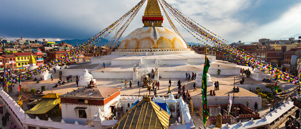 Visitors explore the serene Swoyambhunath Stupa in Kathmandu, surrounded by colorful buildings and prayer flags.