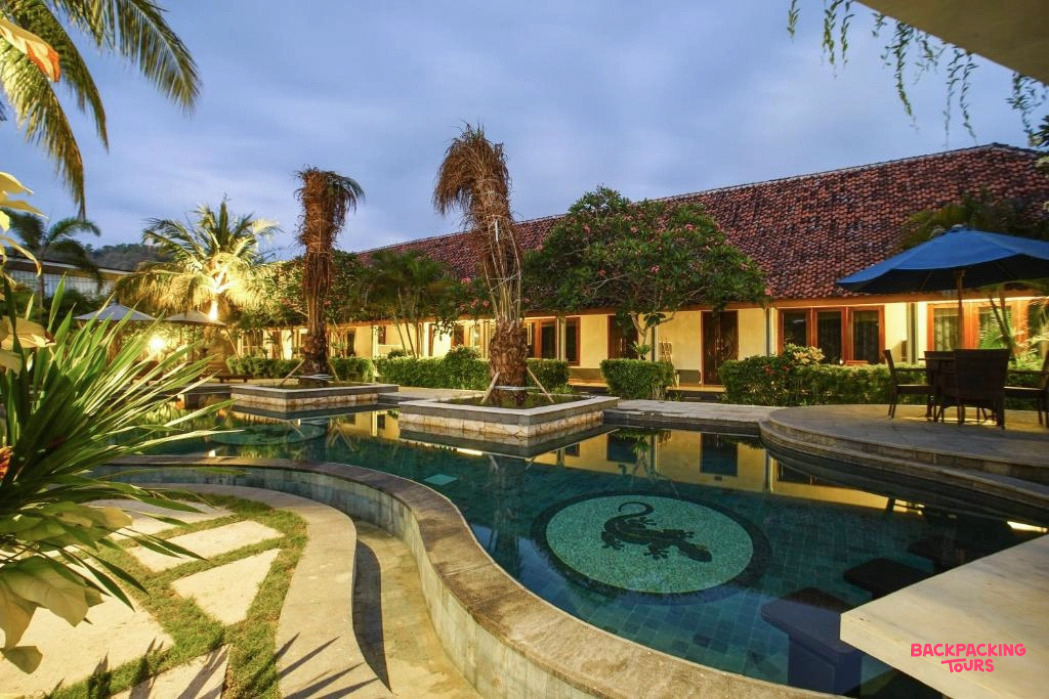 An inviting resort swimming pool with a gecko mosaic and palm trees, lit up at dusk in Lombok.