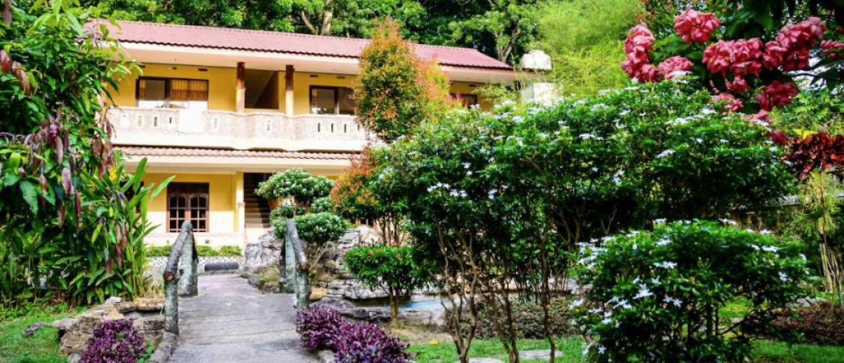 A serene yellow building with a red roof, surrounded by lush tropical gardens in Bukit Lawang.