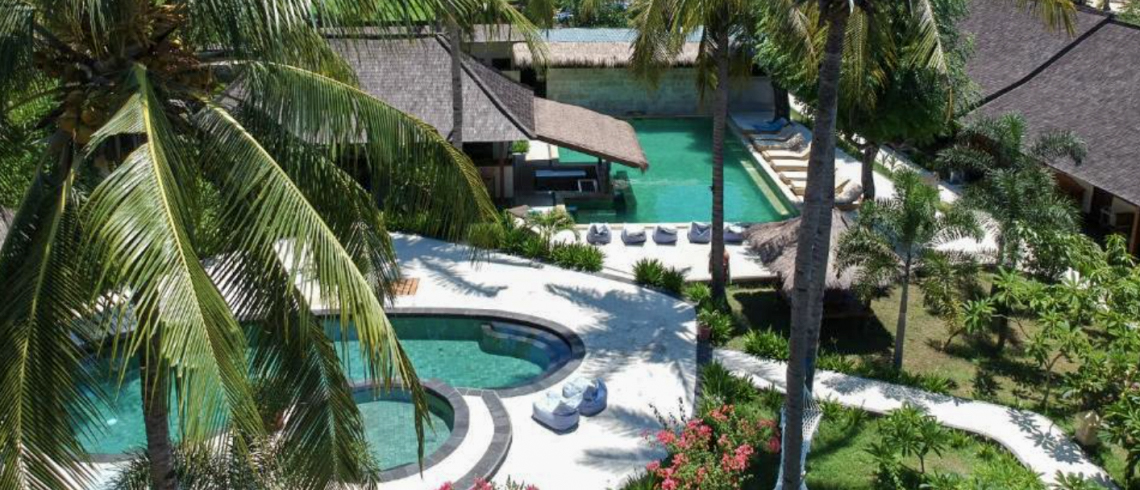 Tropical resort on Gili Trawangan featuring multiple turquoise swimming pools, white pathways, and lush palm trees.
