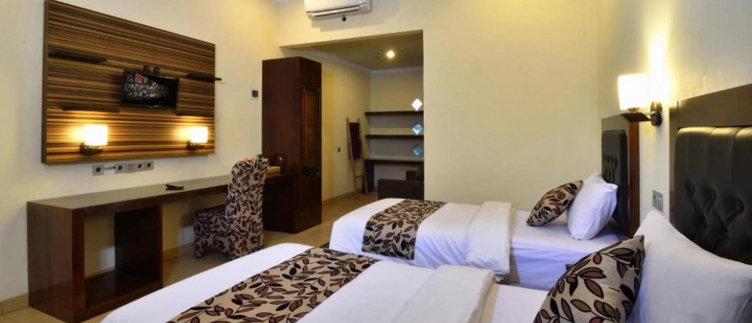 Comfortable hotel room in Lombok featuring two single beds, a desk, and wall-mounted TV.