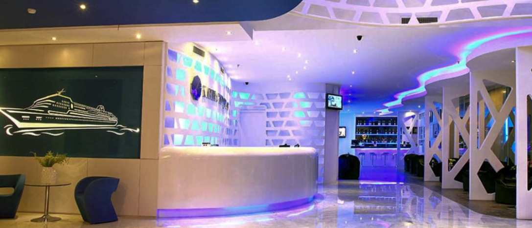 A modern hotel lobby in Medan with a white reception desk and vibrant blue and purple lighting.