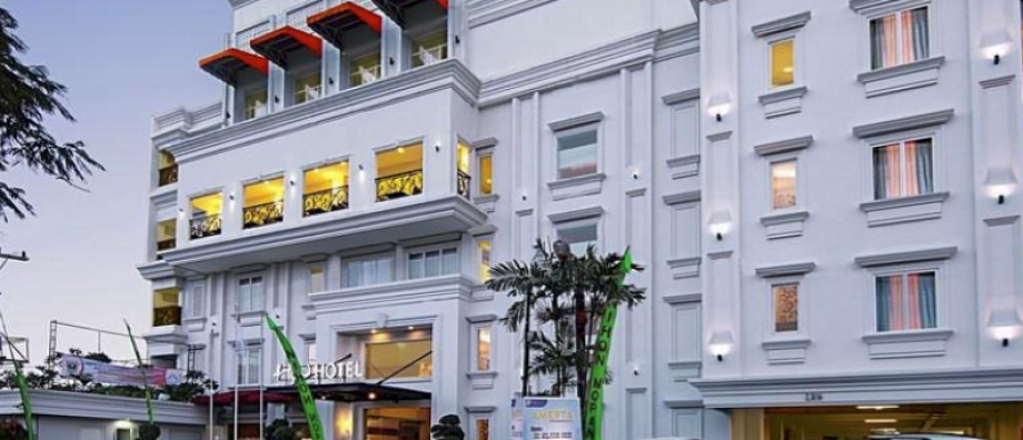 A modern white hotel building with red awnings and illuminated windows in Padang at dusk.