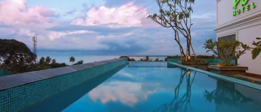 A serene rooftop infinity pool reflects the colorful sunset sky over the ocean in Padang.