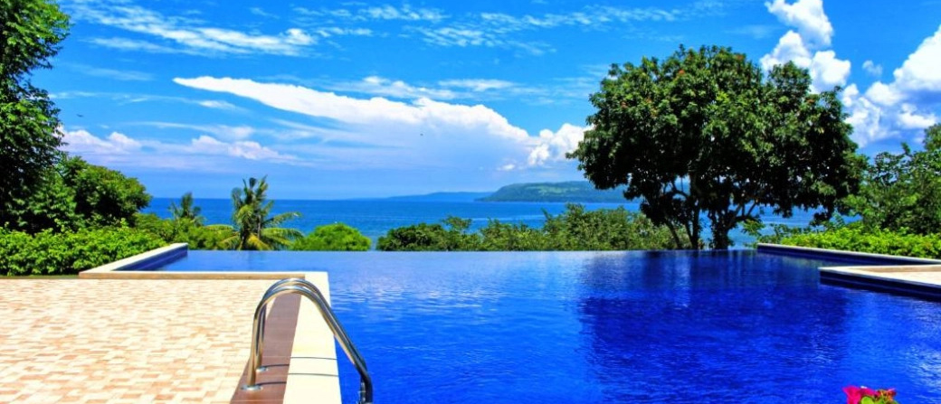 Vibrant blue infinity pool overlooking the tropical ocean and distant coastline of Sumbawa island.