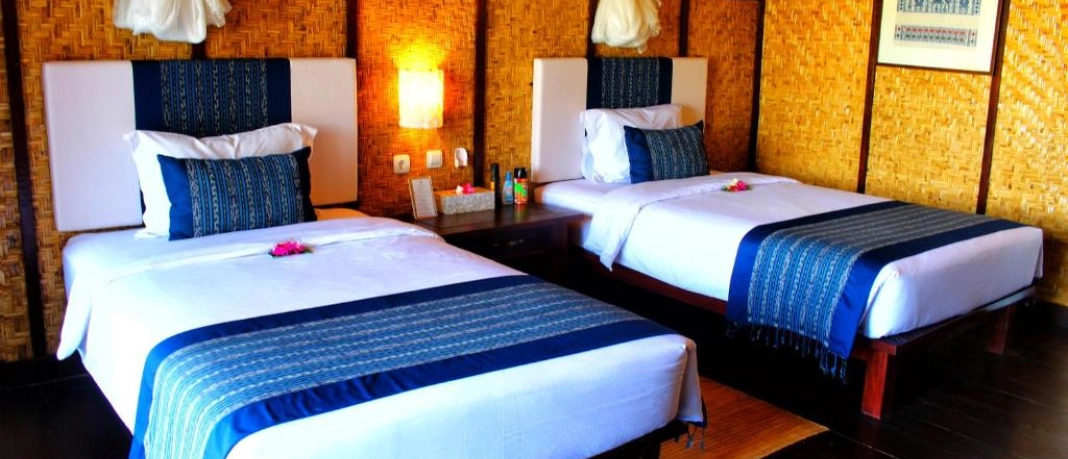 A comfortable twin room with traditional woven walls and blue patterned bedding in Sumbawa.