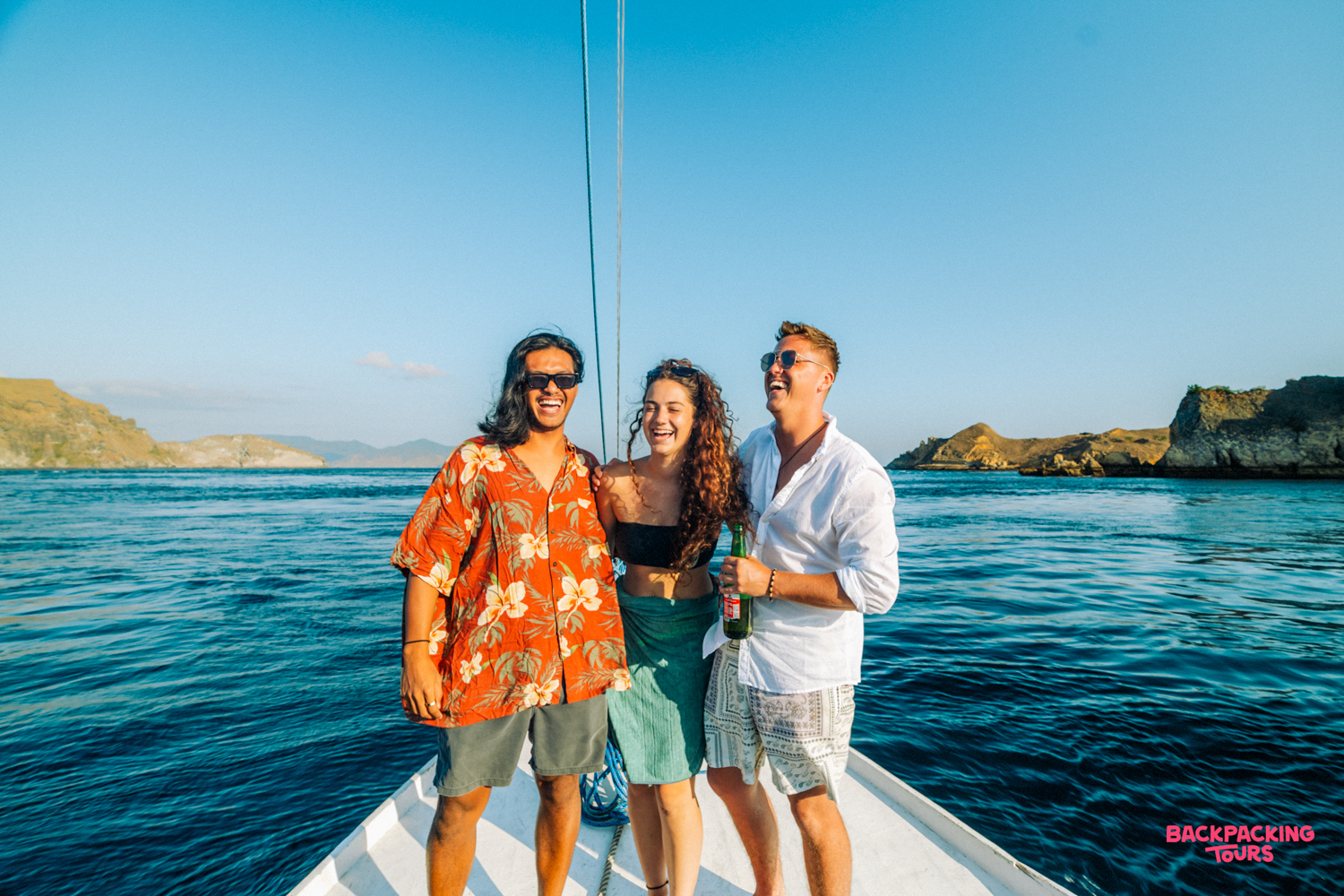 Three smiling friends enjoy a sunny boat trip on the clear blue water near Satonda Island.
