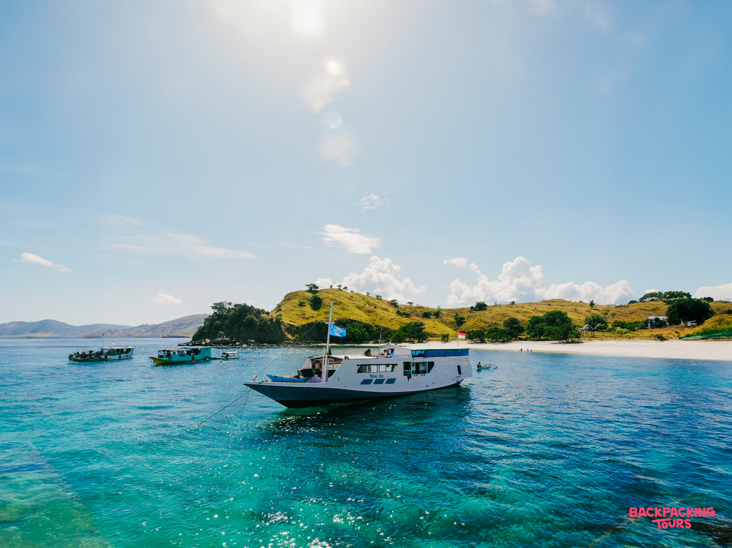 A traditional live-aboard boat anchors in the clear turquoise waters near Satonda Island's white beach.