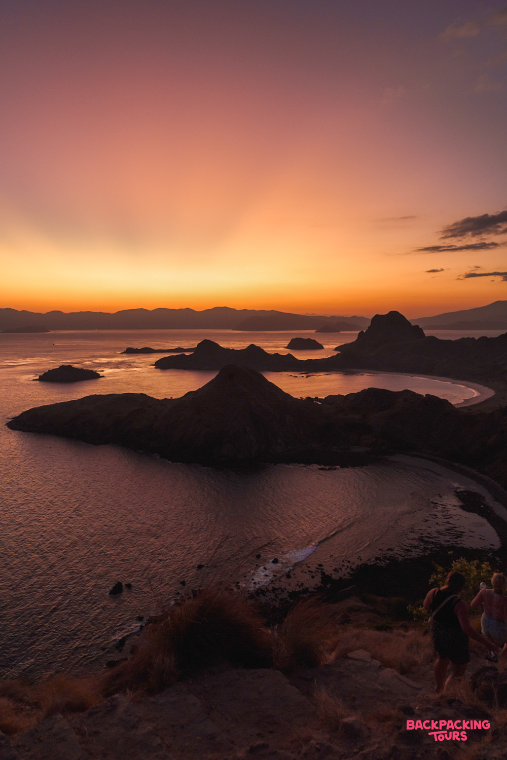 Backpackers enjoy a breathtaking sunset view over the unique island formations of Padar, Indonesia.