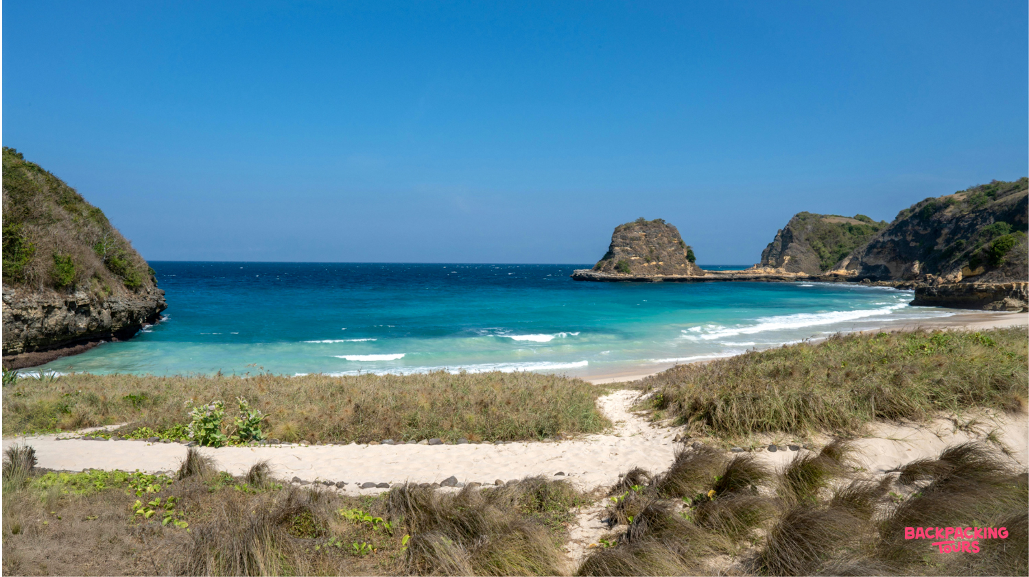 Secluded bay on Lombok featuring clear turquoise water, a sandy beach, and dramatic rocky cliffs.