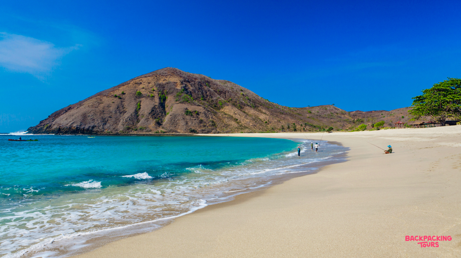 A stunning white sand beach with turquoise water and a large hill under a clear blue sky in Lombok.
