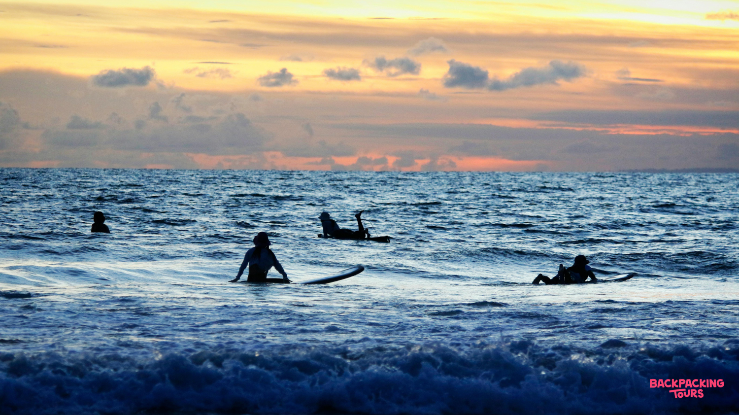 Silhouetted surfers enjoy the beautiful sunset over the calm ocean in Lombok.