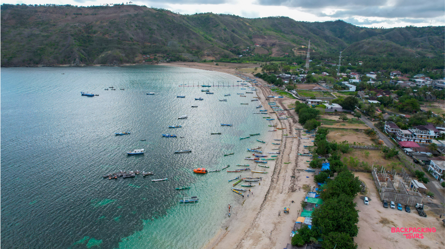 An aerial view of a beautiful bay in Lombok with many traditional boats on the clear turquoise water.