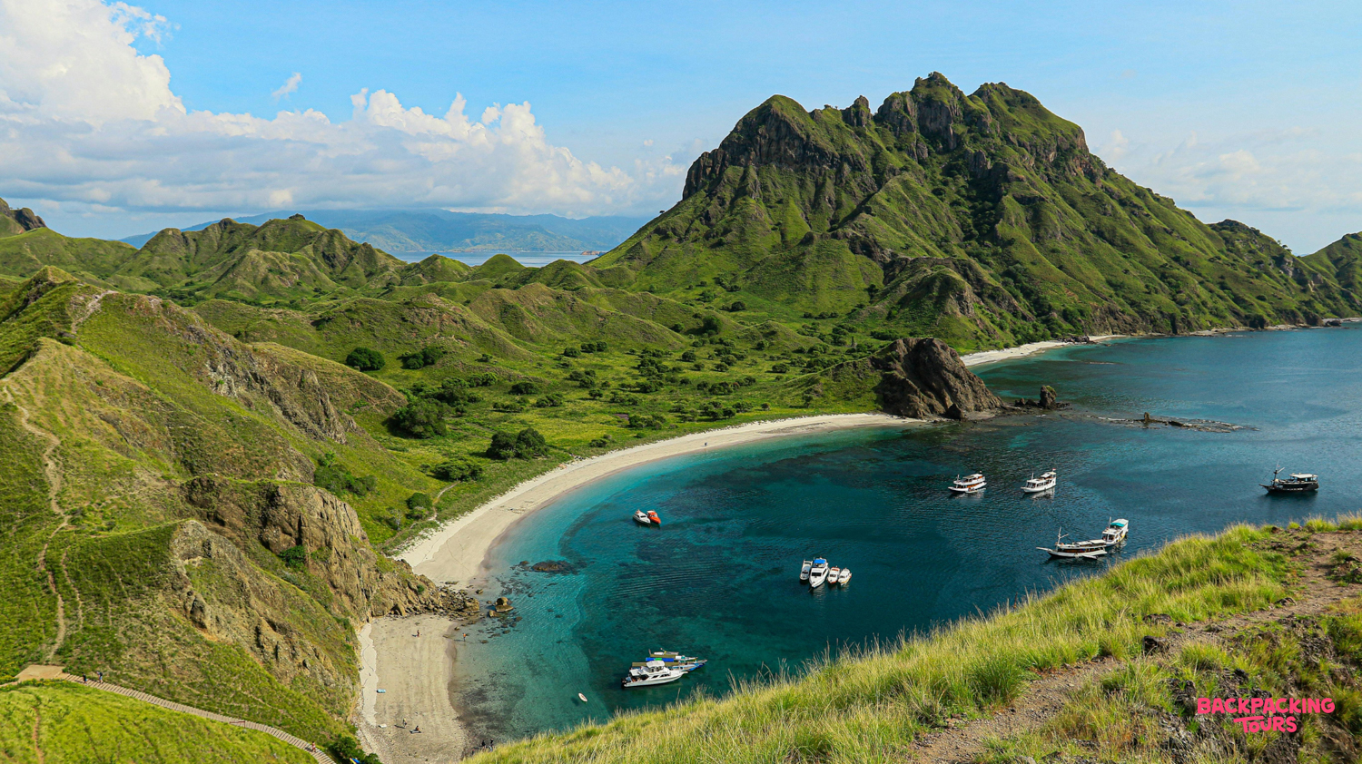 Panoramic view of a pristine turquoise bay with white sand beaches and lush green hills.