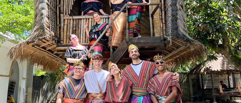 A group of happy travelers wearing traditional Sasak clothing pose in a village in Lombok.
