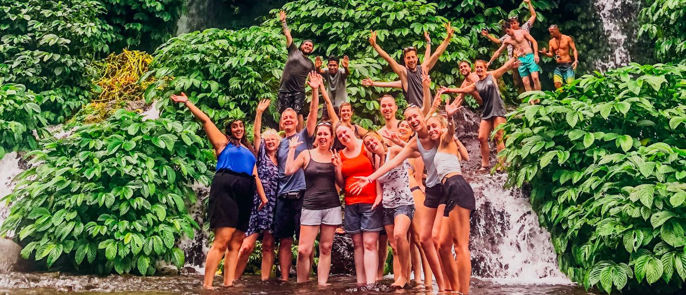 Happy backpackers celebrating in the water at a beautiful waterfall surrounded by green jungle in Lombok.