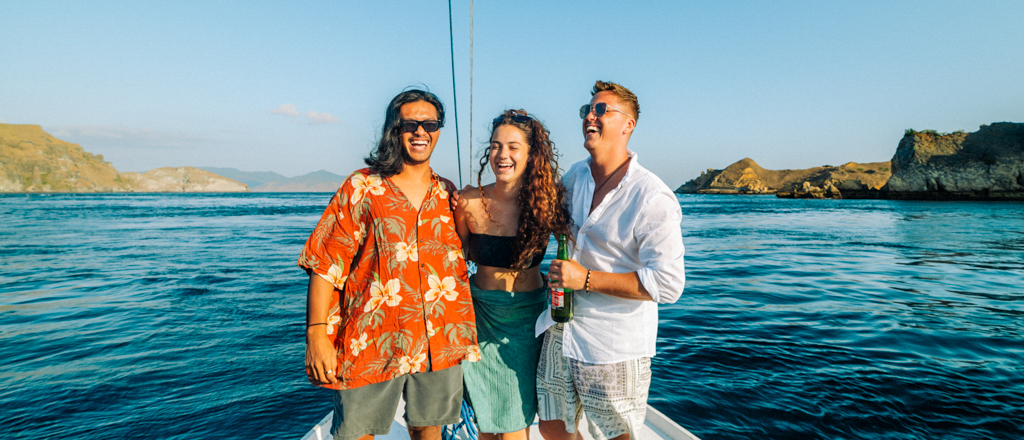 Three happy friends on a liveaboard boat, sailing past Satonda Island, Indonesia on a sunny day.