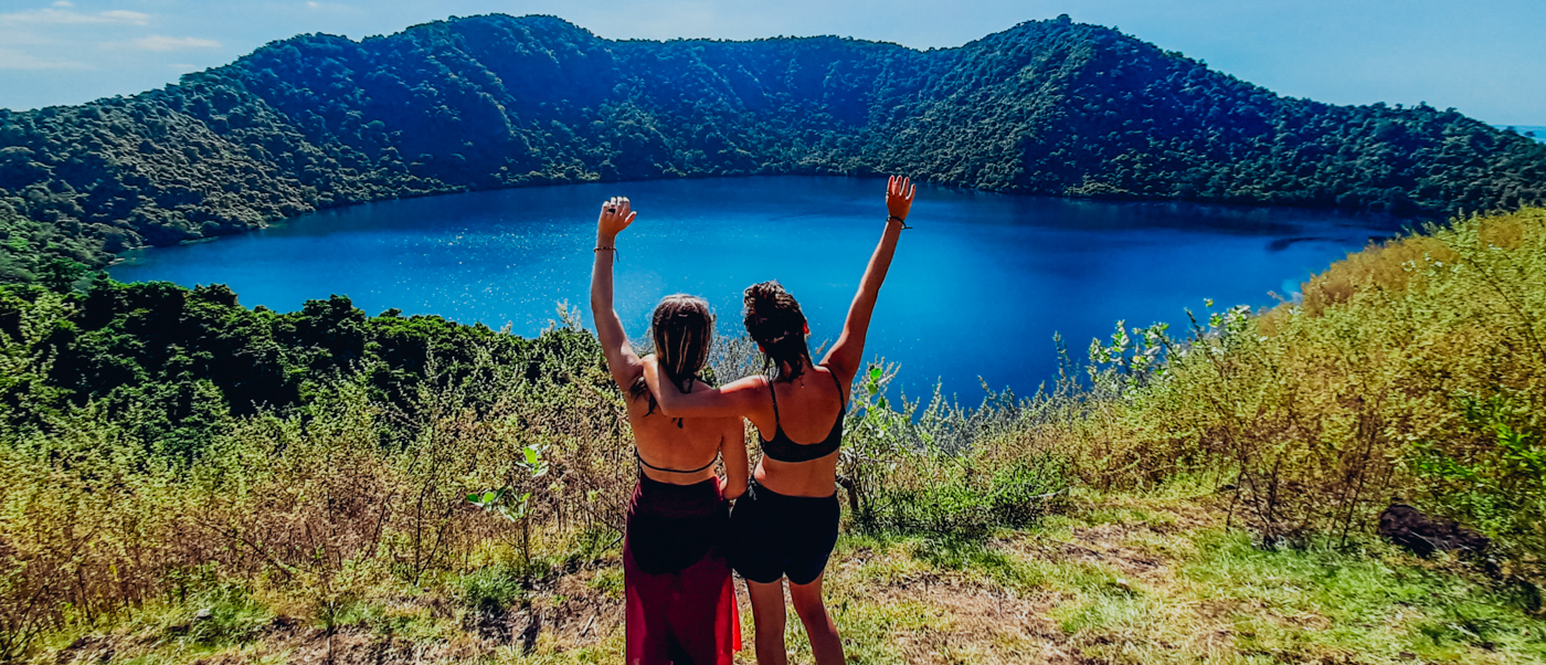 Friends celebrate overlooking the vibrant blue crater lake surrounded by green hills on Satonda Island.