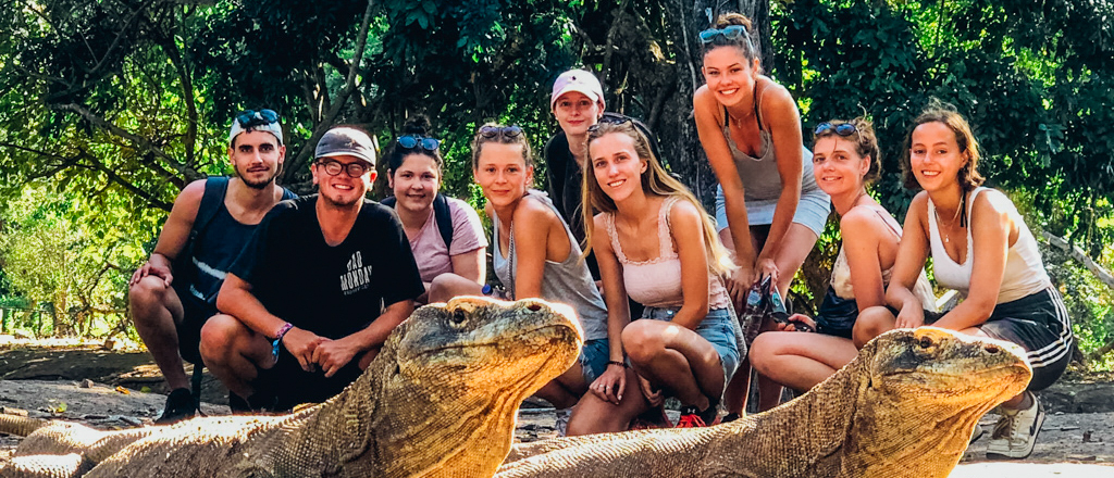 A happy group of backpackers crouches behind two large Komodo dragons on Komodo Island.