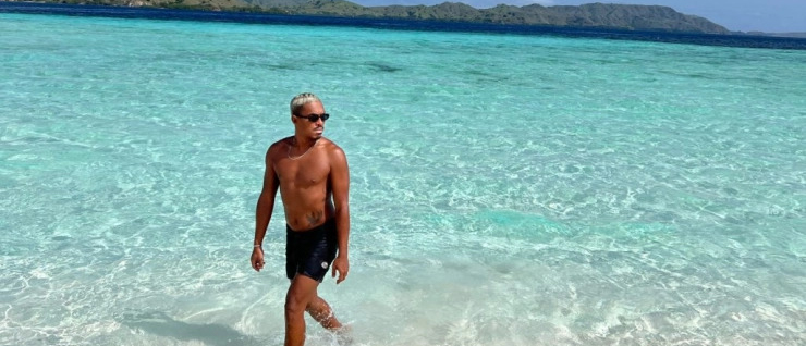 A man walks out of the incredibly clear turquoise water on a sunny beach in Lombok.