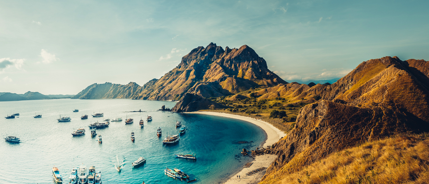 Beautiful bay with many boats, a white beach, and golden hills in Komodo National Park.