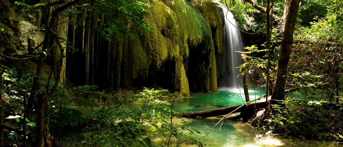 A beautiful waterfall plunges into a clear turquoise pool amidst dense green jungle on Moyo Island.