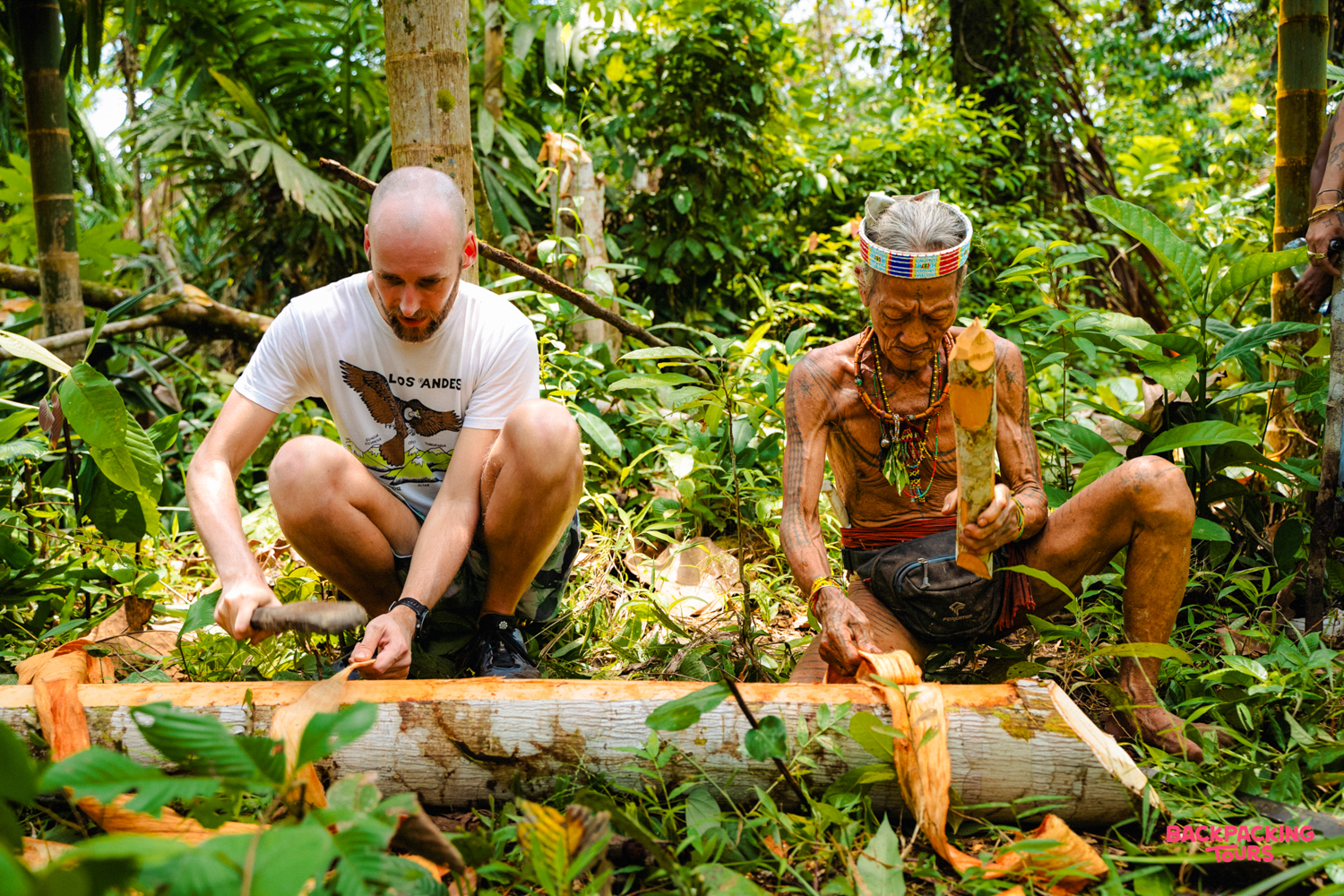 A traveler learns traditional wood carving from a Mentawai tribesman in the Indonesian jungle.