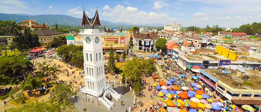 A bustling Padang city square with a distinctive white clock tower and a vibrant market.